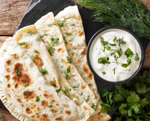 Typical-Turkish-meal-Gozleme-with-herb-and-cheese-on-slate-board-on-the-table.-Horizontal-top-view-from-abov-min Typical-Turkish-meal-Gozleme-with-herb-and-cheese-on-slate-board-on-the-table.-Horizontal-top-view-from-abov-min